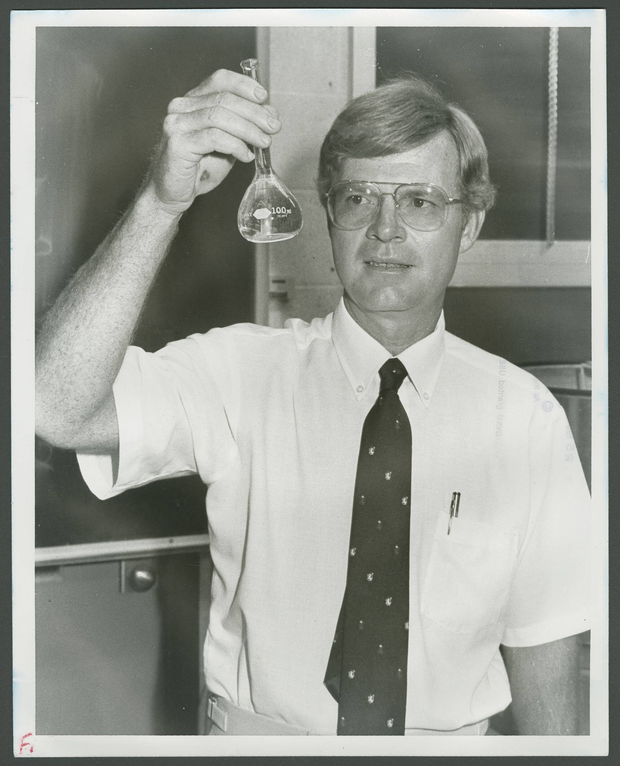 AWRI's first director, Ron Ward, holds up and examines a 100 mL volumetric flask.